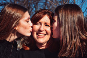 Two you girls kissing their mother on each cheeck